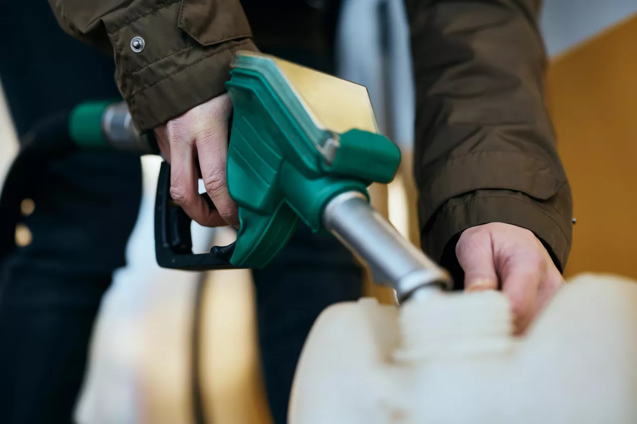 Close-up of woman filling plastic gallon with fuel at a gas station.