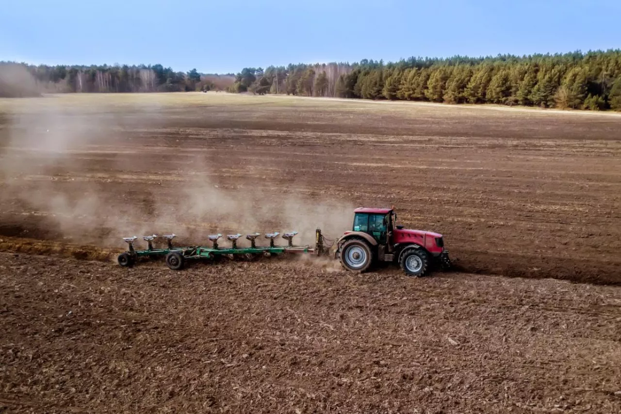 Ciągnik rolniczy wykonujący orkę pola uprawnego z wykorzystaniem pługa wieloskibowego. Widok z góry na prace polowe na dużej powierzchni gruntu.